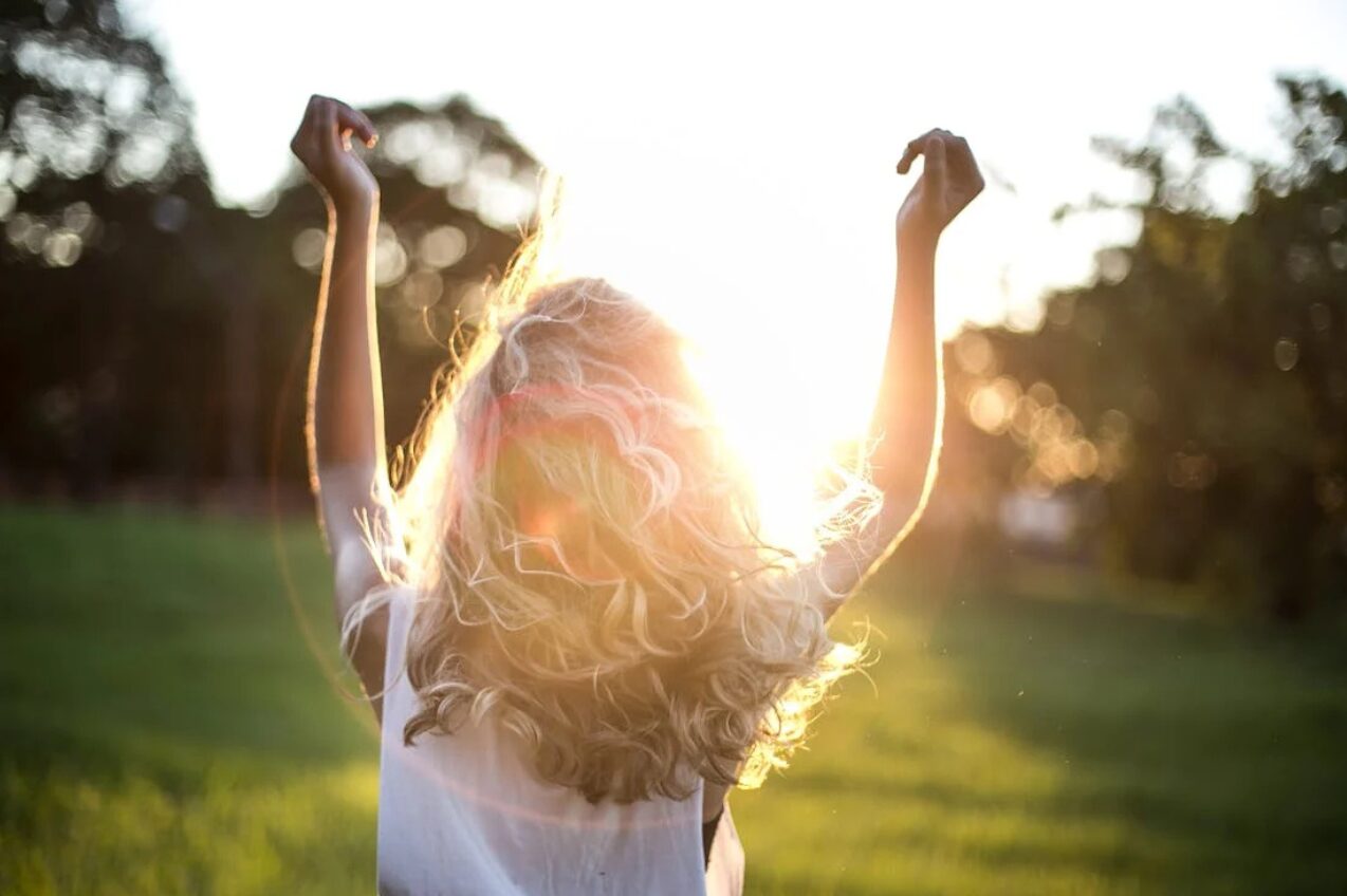 Back view of a woman raising her arms in a sunlit field, symbolizing women’s health and wellness